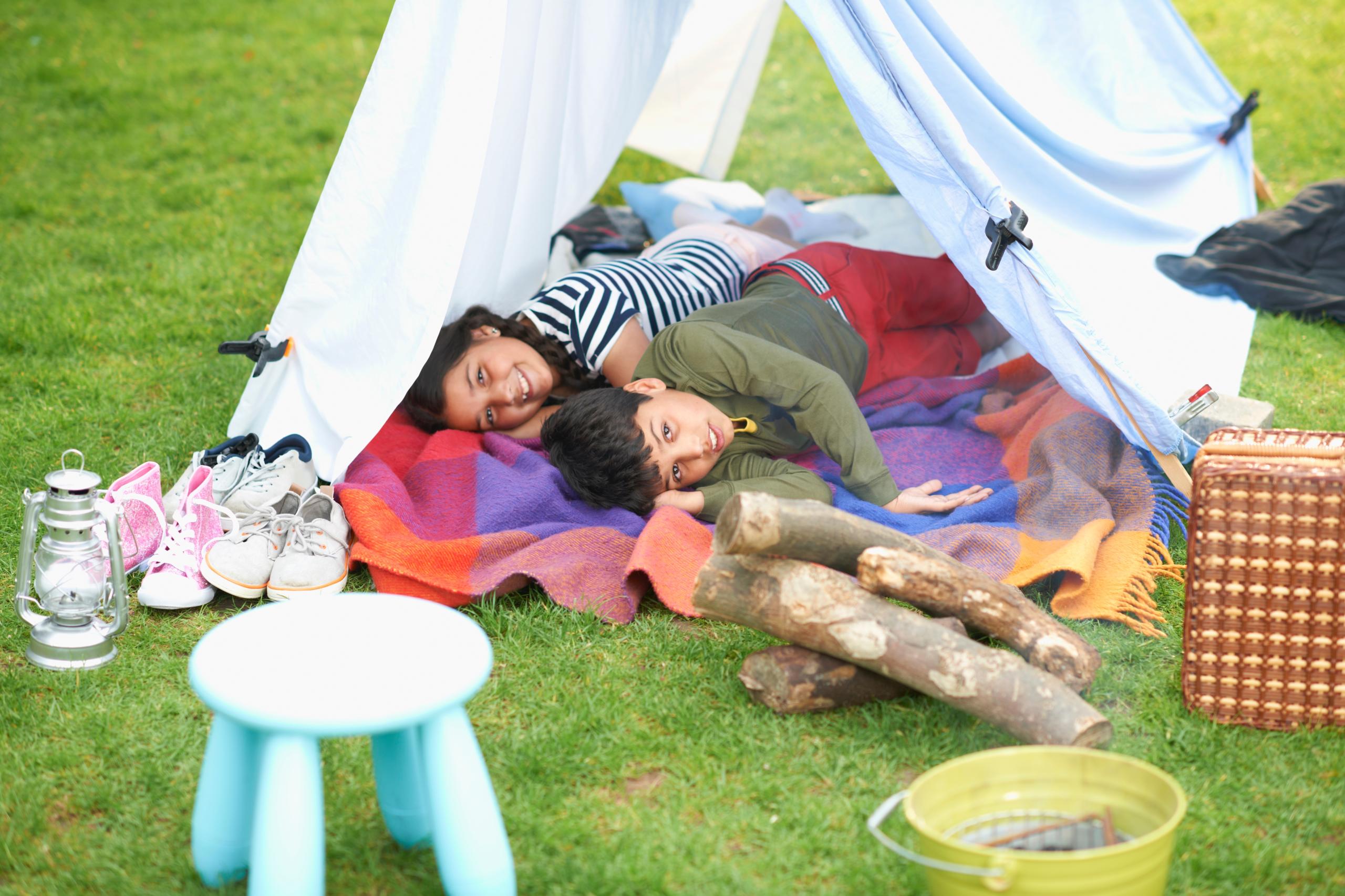 Brother and sister lying in homemade tent in backyard.