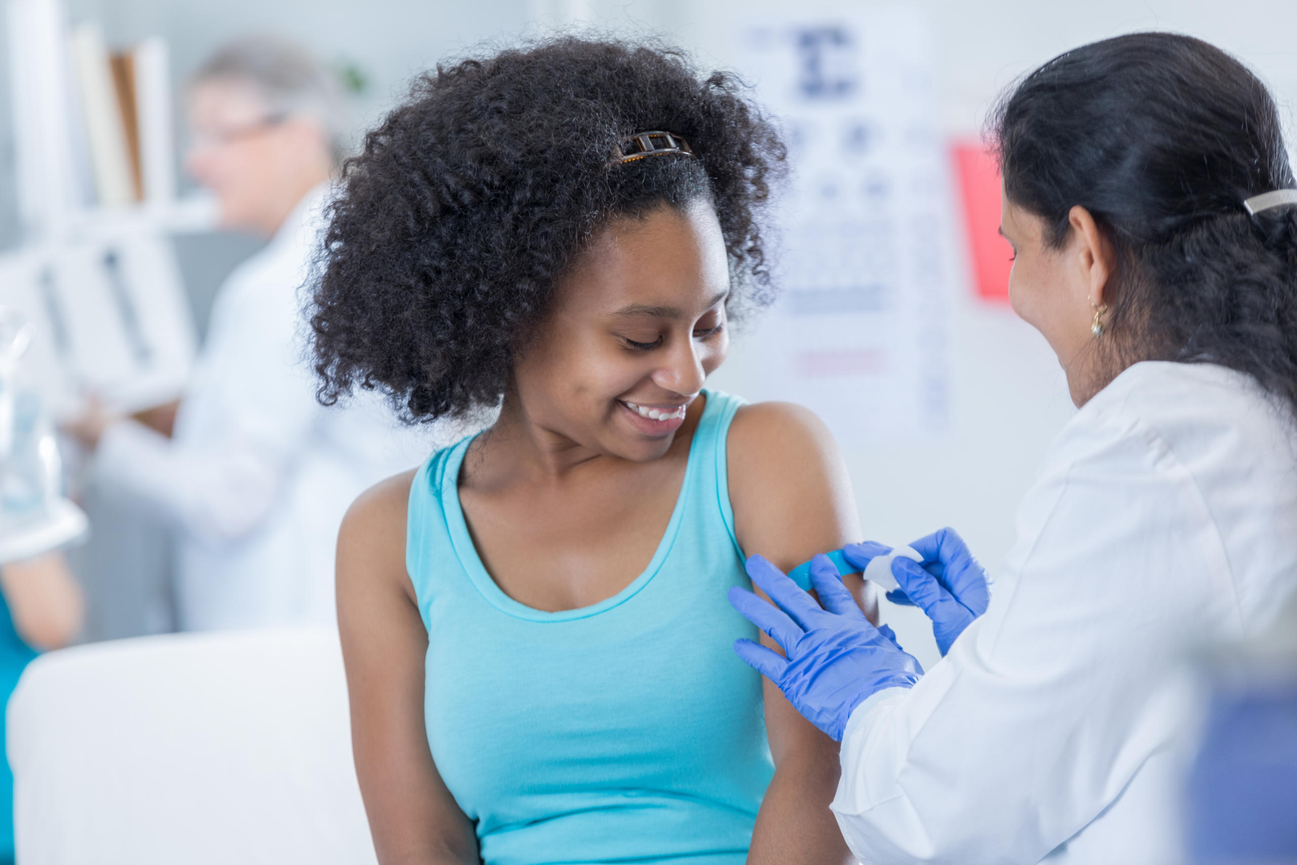 Female doctor places a bandage on teenage female patient's arm.