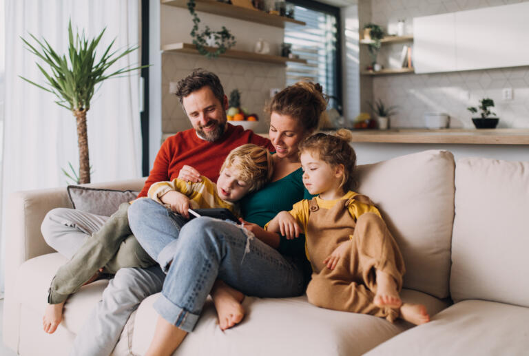 Little children bonding with parents on sofa at home and using tablet