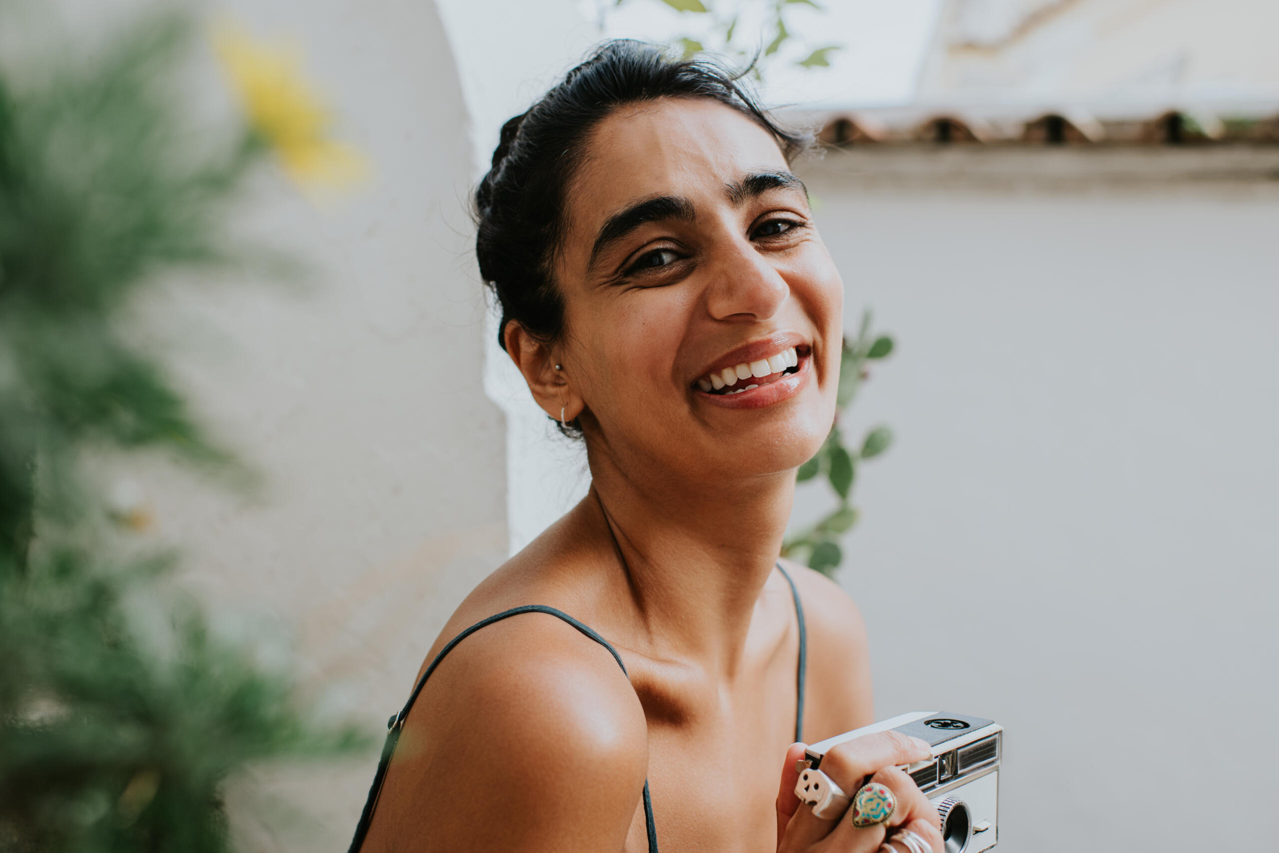 Simple portrait of a confident young Indian woman outside, looking directly at the camera. She looks confident, and relaxed. She holds a vintage film camera.