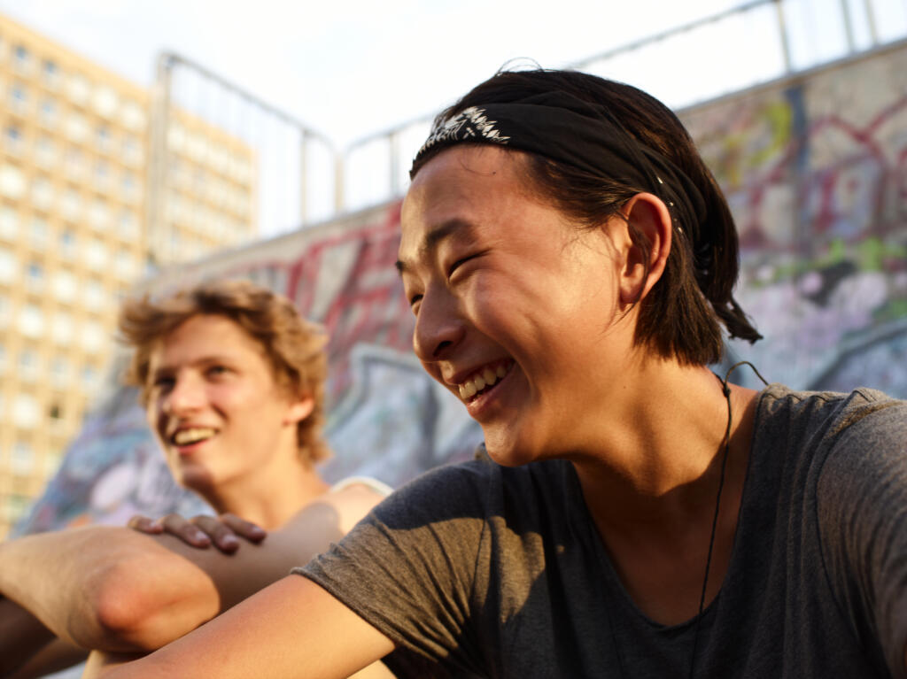 Two people sit in front of a graffitied skateboard ramp, laughing together.