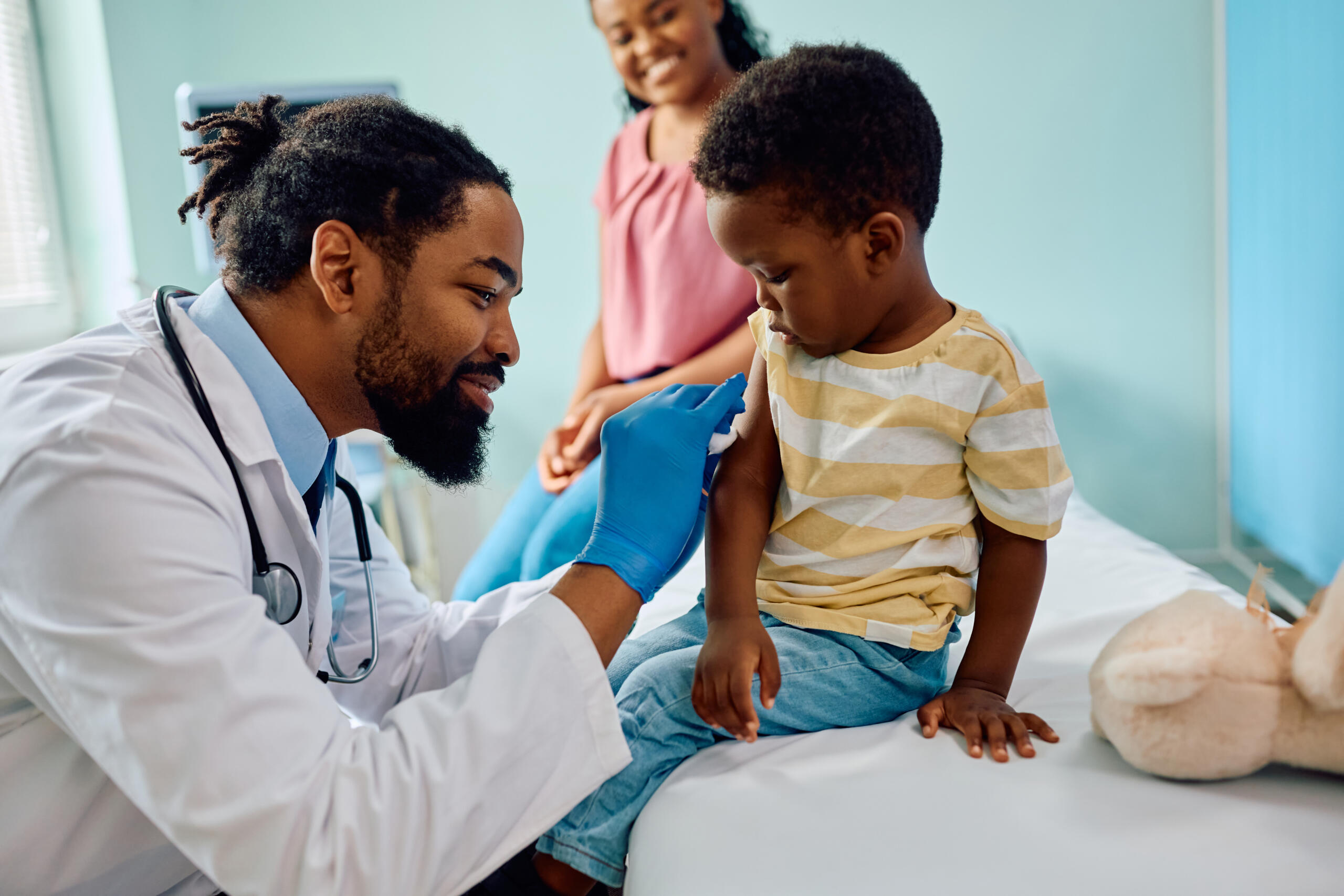 Doctor gently preps a child’s arm for blood draw as a parent smiles and watches.